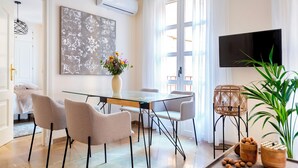 A modern dining area with a glass table, four chairs, a vase with flowers, a television, and a plant. - Genteel Home Reyes Católicos (Granada)