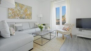 A modern living room with a sofa, coffee table, armchair, and TV. - The Best Location, 8pax, 3BD & 2Bth, Reina Sofia II (Madrid)