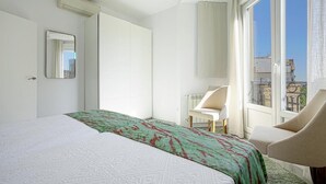A hotel room with a large bed, a chair, a window with a view of buildings, and a mirror on the wall. - The Best Location, 8pax, 3BD & 2Bth, Reina Sofia II (Madrid)