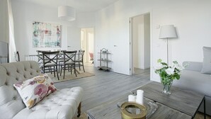 A modern living room with a sofa, coffee table, and a dining area with chairs and a table. - The Best Location, 8pax, 3BD & 2Bth, Reina Sofia II (Madrid)