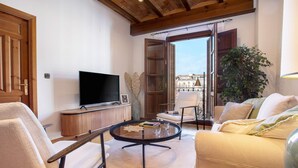 Una sala de estar con televisor, una mesa redonda, un sofá y un ventanal con vistas a edificios.