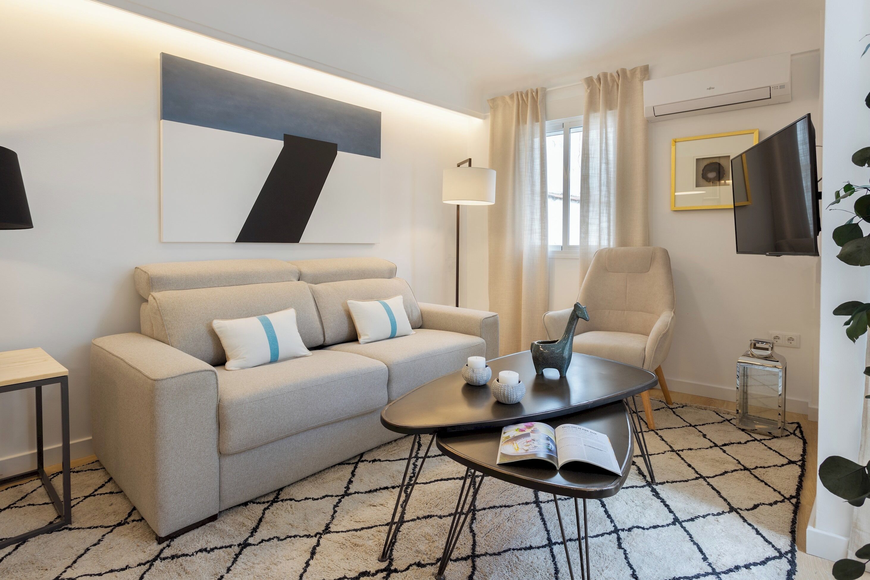 Ein modernes Wohnzimmer mit einer Couch, einem Sessel, einem Couchtisch und einem an der Wand befestigten Fernseher.