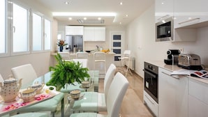 A modern kitchen with white cabinets, a stainless steel oven, and a microwave. There is a dining area with a glass table and white chairs. - Genteel Home Recogidas (Granada)