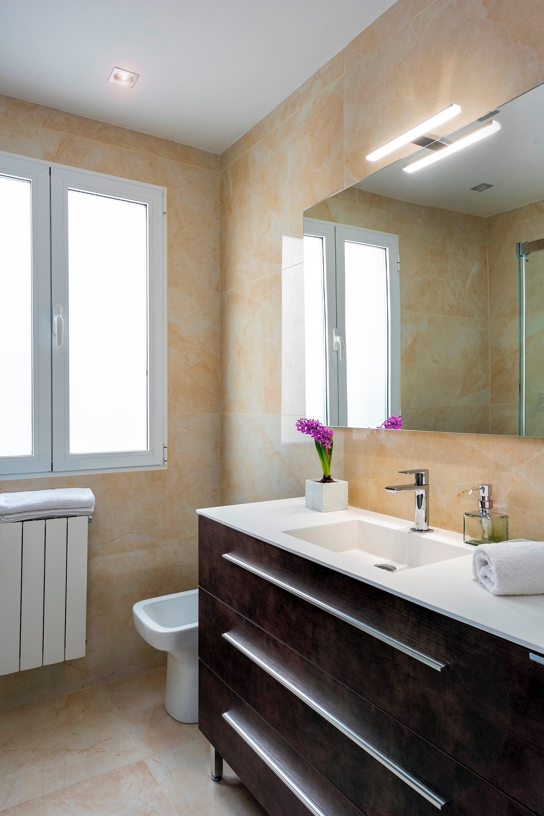 A modern bathroom with a white vanity, a large mirror, and a window.