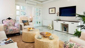A modern living room with a sofa, armchair, and coffee table, a television, and a cabinet with decorative items. - Genteel Home Recogidas (Granada)