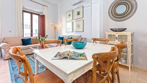 A dining area with a white table, wooden chairs, and a blue bowl. There are framed pictures on the wall and a cabinet with glass doors. - Genteel Home Arfe Terrace II (Seville)