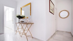 Un pasillo con una puerta blanca, un espejo redondo y una pequeña mesa con un florero.