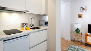 A modern kitchen with white cabinets, a stainless steel range hood, a built-in microwave, and a sink. There are lemons on the counter, and a small table with a lamp and a picture frame. - Genteel Home Santo Cristo (Granada)