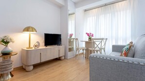 A modern living room with a flat-screen TV, a wooden cabinet, a round side table, a grey sofa, and a dining area with a small table and chairs. - Genteel Home Santo Cristo (Granada)