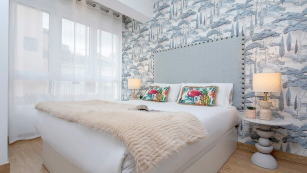 A bedroom with a large bed, two bedside lamps, a fluffy throw blanket, and a wall with a nature-themed wallpaper. - Genteel Home Santo Cristo (Granada)