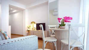 A modern living room with a sofa, two white chairs, a small round table with a potted plant, and a flat-screen TV. - Genteel Home Santo Cristo (Granada)