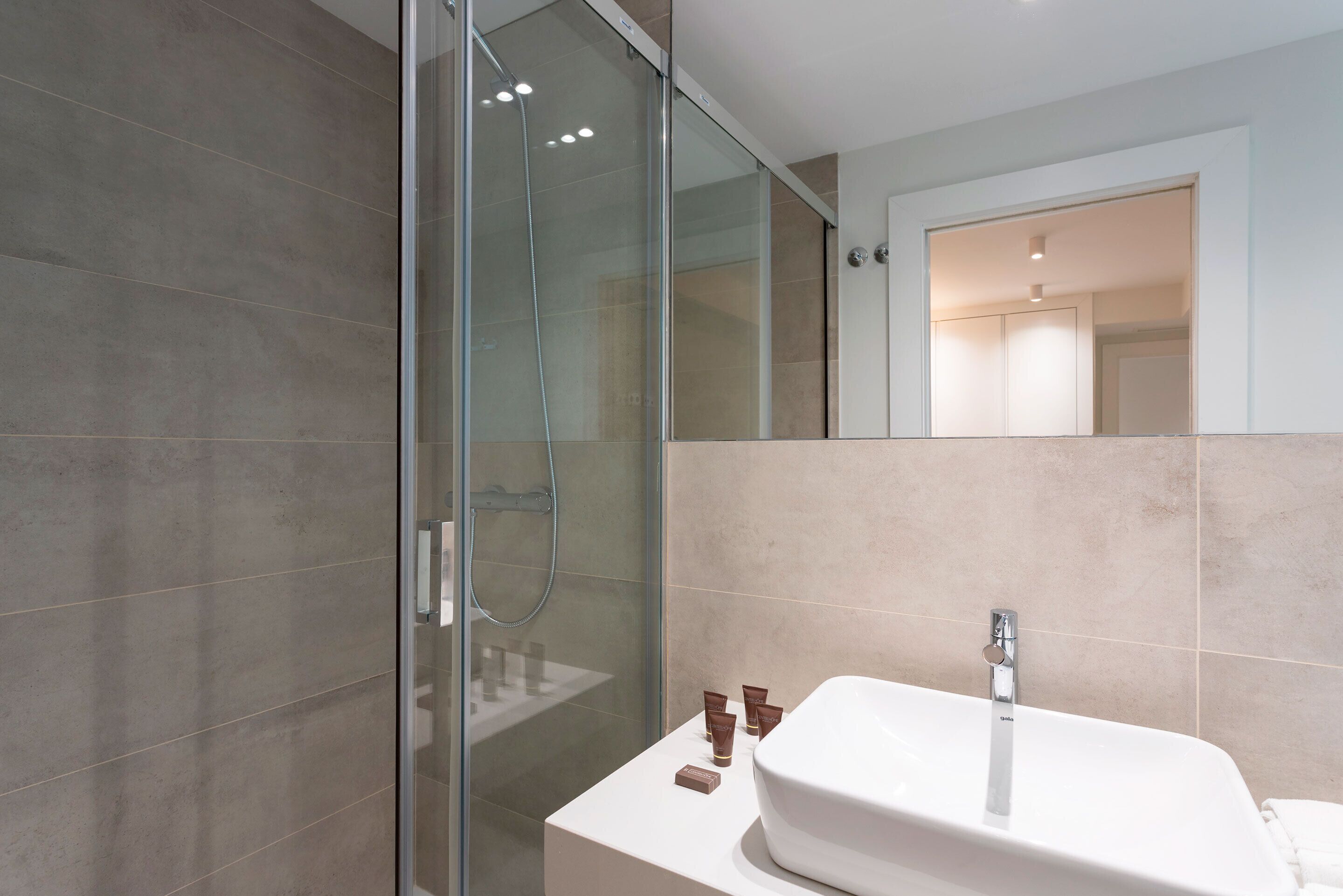 A modern bathroom with a glass-enclosed shower, a white sink, and a mirror.