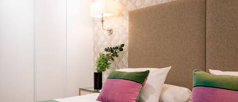 A hotel room with a bed, pillows, a nightstand, a lamp, and a plant.
