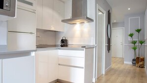 A modern kitchen with white cabinetry, a built-in stove, and a stainless steel range hood. - Genteel Home Amira (Granada)