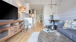 A modern living room with a flat-screen TV, wooden entertainment unit, grey sofa, patterned coffee table, and a dining area with chairs and a table. - Genteel Home Amira (Granada)