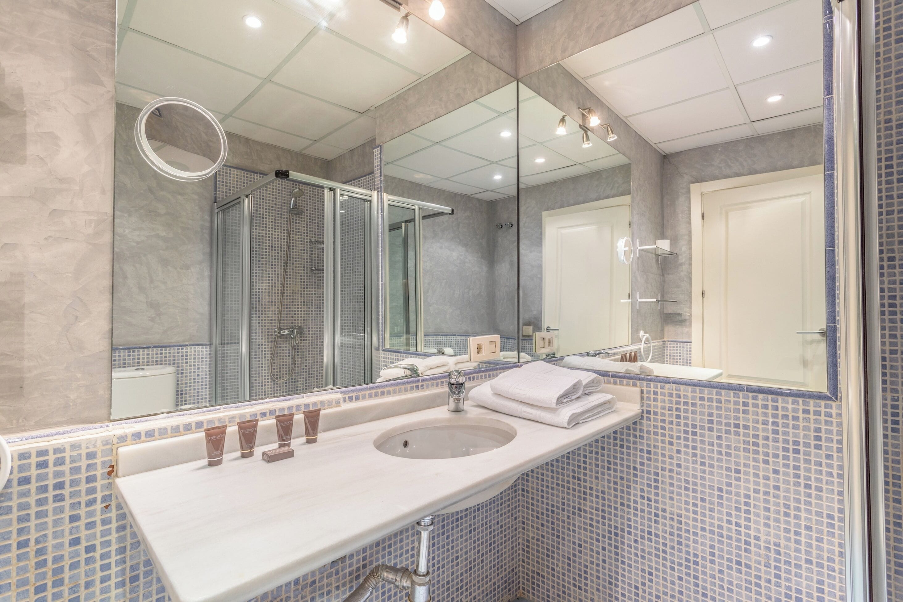 A modern bathroom with a large mirror, a sink with toiletries, and a shower area.