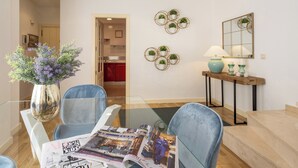 A modern living room with a glass coffee table, two blue armchairs, a wooden side table with a lamp, and decorative wall art. - Genteel Home Francos Terrace VI (Seville)