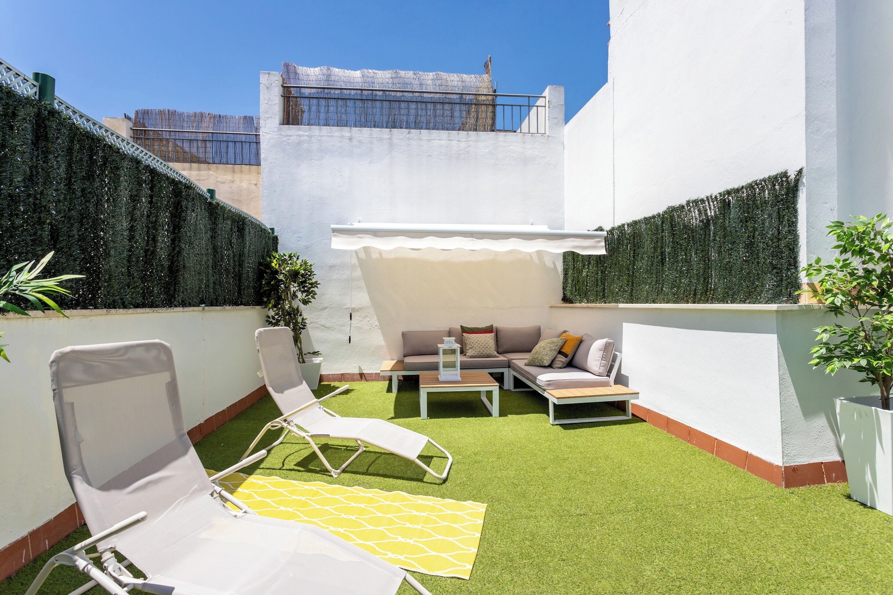A rooftop patio with artificial grass, a sofa set, and two lounge chairs.