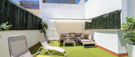 A rooftop patio with artificial grass, a sofa set, and two lounge chairs.