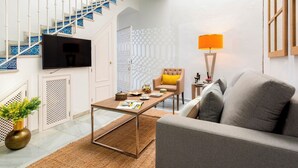 A living room with a sofa, a coffee table, a TV mounted on the wall, a staircase with blue tiles, and a patterned wall. - Genteel Home Argote de Molina (Seville)