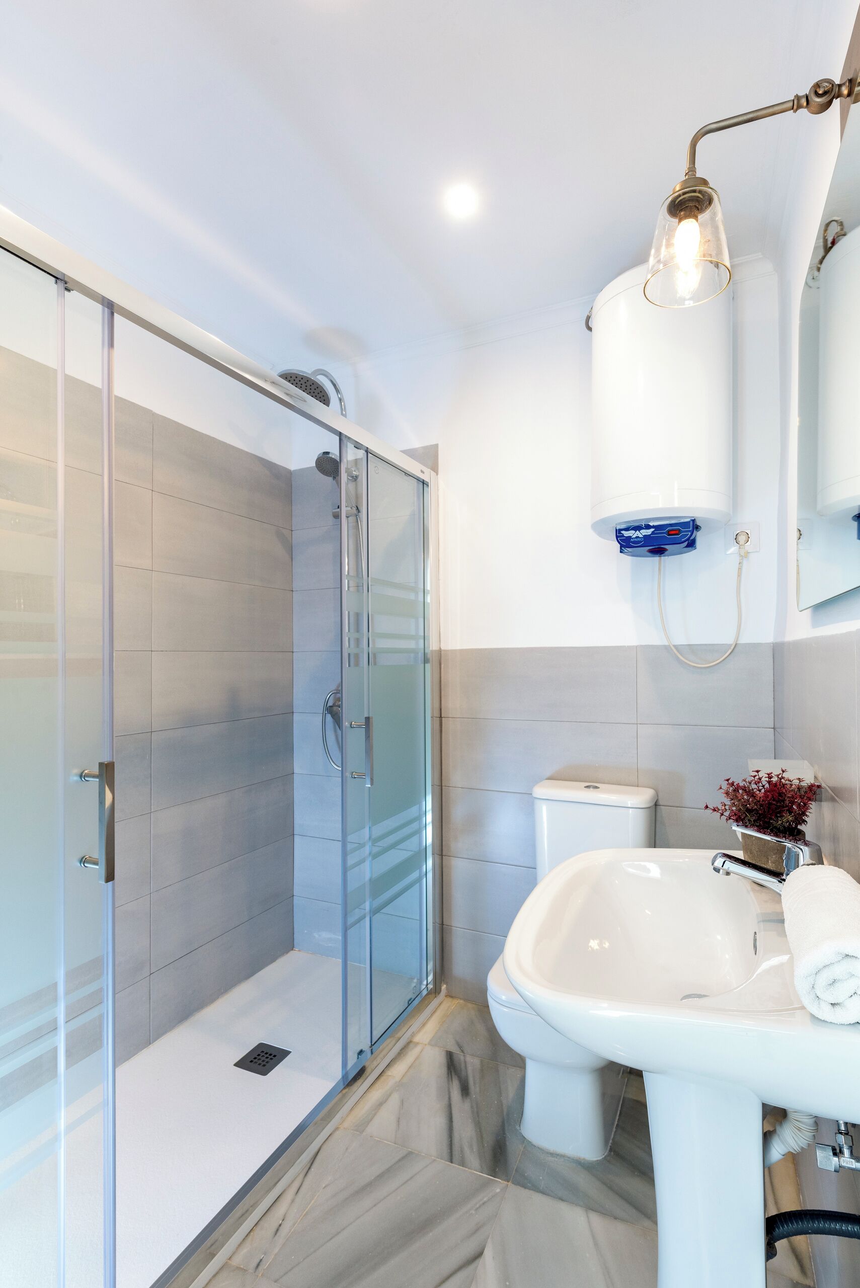 A modern bathroom with a glass shower enclosure, a white sink, and a wall-mounted light fixture.