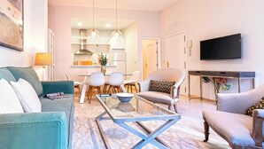 A modern living room with a sofa, coffee table, and chairs, a dining area with a table and chairs, a kitchen in the background, and a TV mounted on the wall. - Genteel Home Arfe Terrace (Seville)