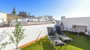 A rooftop terrace with lounge chairs, a small table, and a potted plant. - Genteel Home Arfe Terrace (Seville)