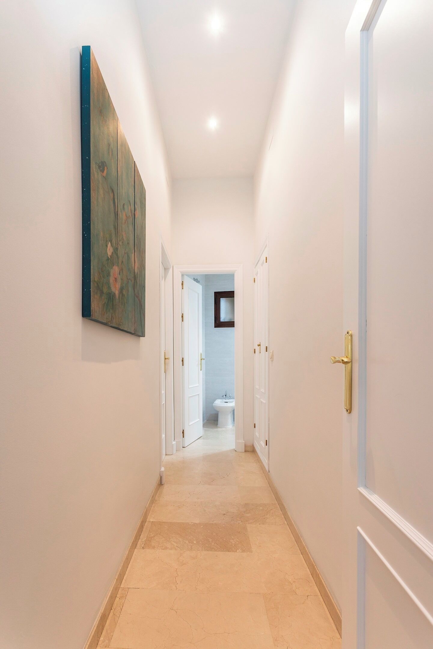 Un couloir avec un tableau, des portes blanches et une vue sur une salle de bain.