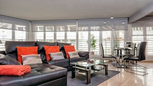 Ein modernes Wohnzimmer mit einer schwarzen Ledersofa, einem Glastisch und einem Essbereich mit schwarzen Stühlen und einem Glastisch.