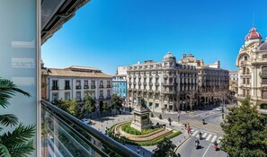 Une place de ville bordée de bâtiments historiques, un monument central et un ciel d’un bleu éclatant.