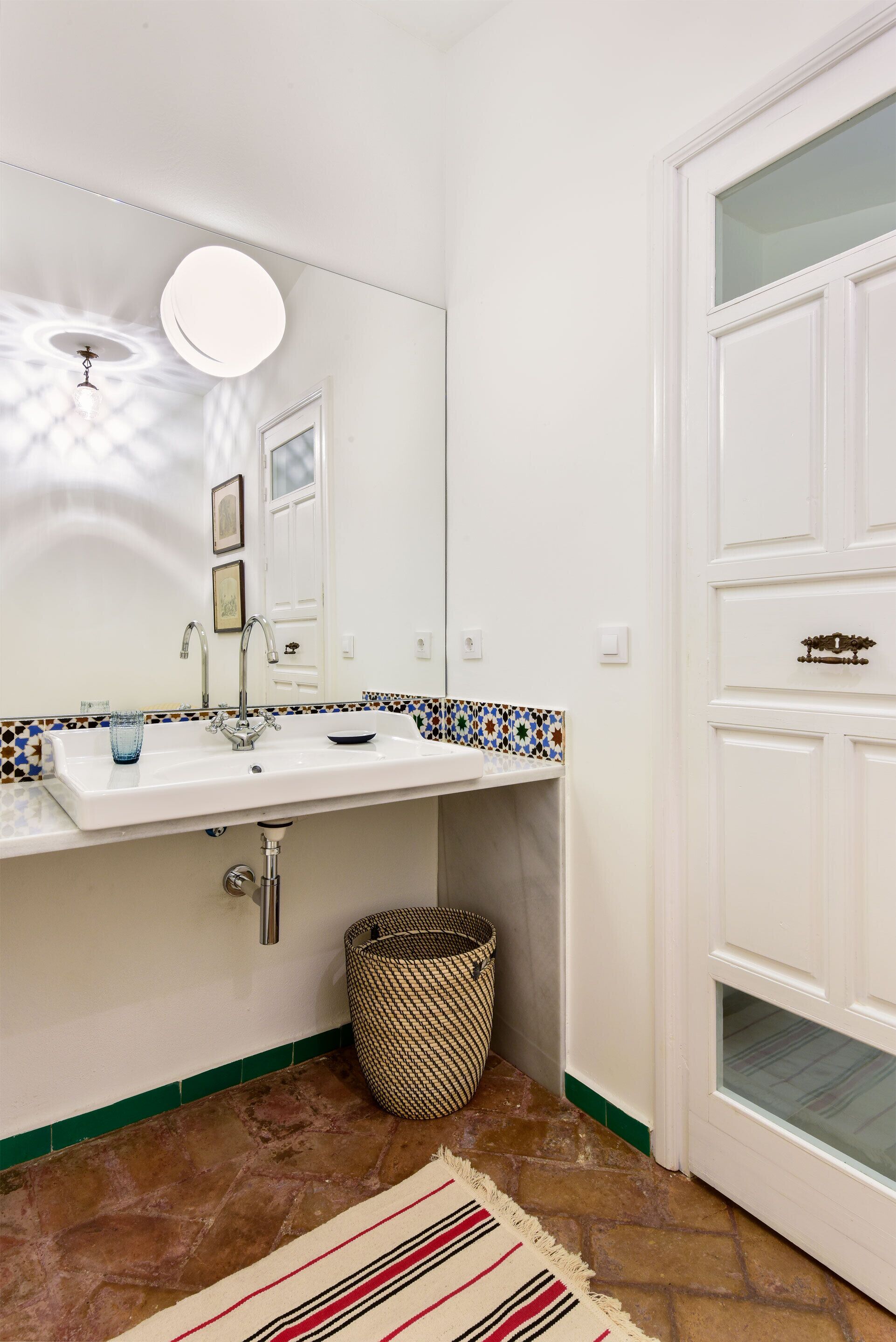 Un baño con lavamanos blanco, espejo y salpicadero de azulejos.