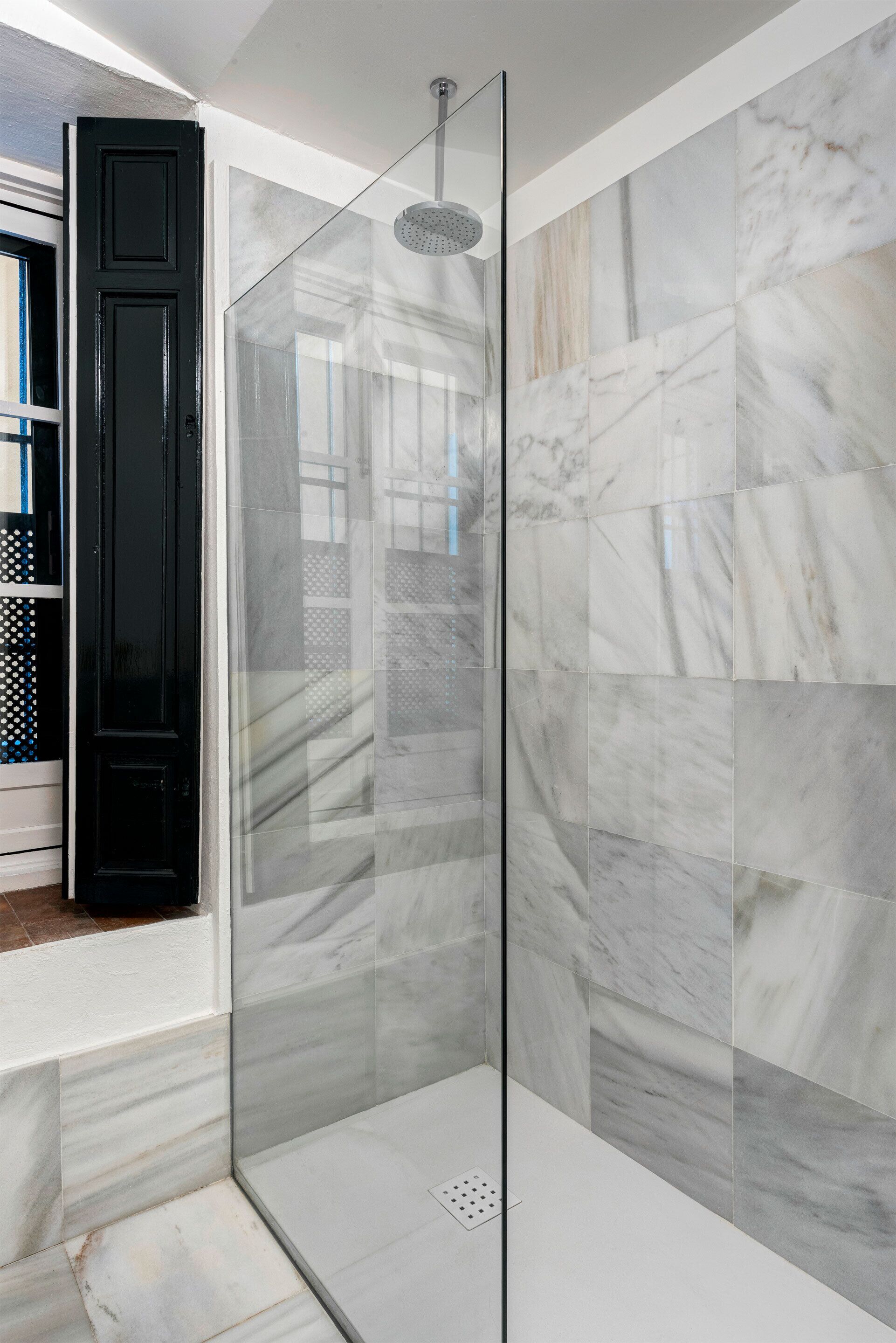 A glass-enclosed shower with marble tiles and a black door.