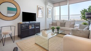 A modern living room with a glass coffee table, a sofa, a TV, and a large window offering a view of the outdoors. - Genteel Home Campana (Seville)