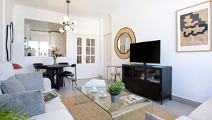 A modern living room with a glass coffee table, a sofa, a TV, and a black entertainment unit. - Genteel Home Campana (Seville)
