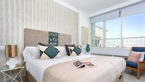 A modern hotel room with a large bed, striped bedding, and a view of the city through large windows. - Genteel Home Campana (Seville)