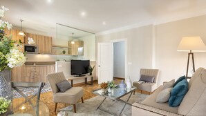 A modern living room with a glass coffee table, beige sofas, and a television.