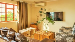 A living room with a leather sofa, a patterned armchair, a wooden coffee table, and a large window with curtains. - Sun & Sea Family Villa (Cape Town)