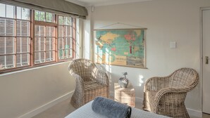 A room with a large window, wicker chairs, a bed with a rolled-up blanket, and a world map on the wall. - Sun & Sea Family Villa (Cape Town)