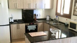 Een moderne keuken met houten kastjes, een zwart aanrecht, een ingebouwde oven, een magnetron en een spoelbak.