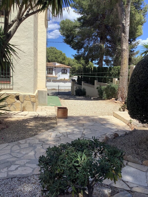 Un patio con un camino de piedra, un pequeño arbusto y un edificio con tejado de baldosas.
