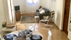 Een eetgedeelte met een ronde tafel voor vier personen, een bank en een televisie op de achtergrond.