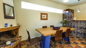 Zona pranzo con tavolo in legno, sedie blu, base blu, piastrelle a parete, uno specchio e un quadro incorniciato.