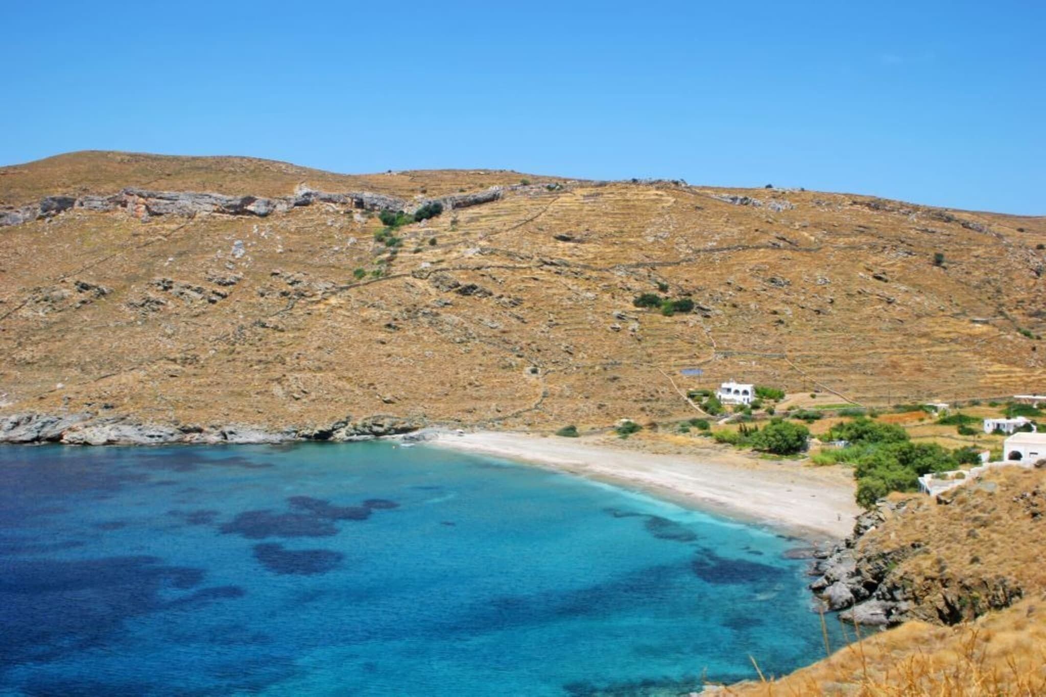A coastal landscape with a beach, rocky hills, and a few buildings.