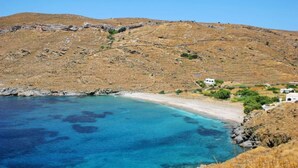 Paesaggio costiero con spiaggia, colline rocciose e alcuni edifici.