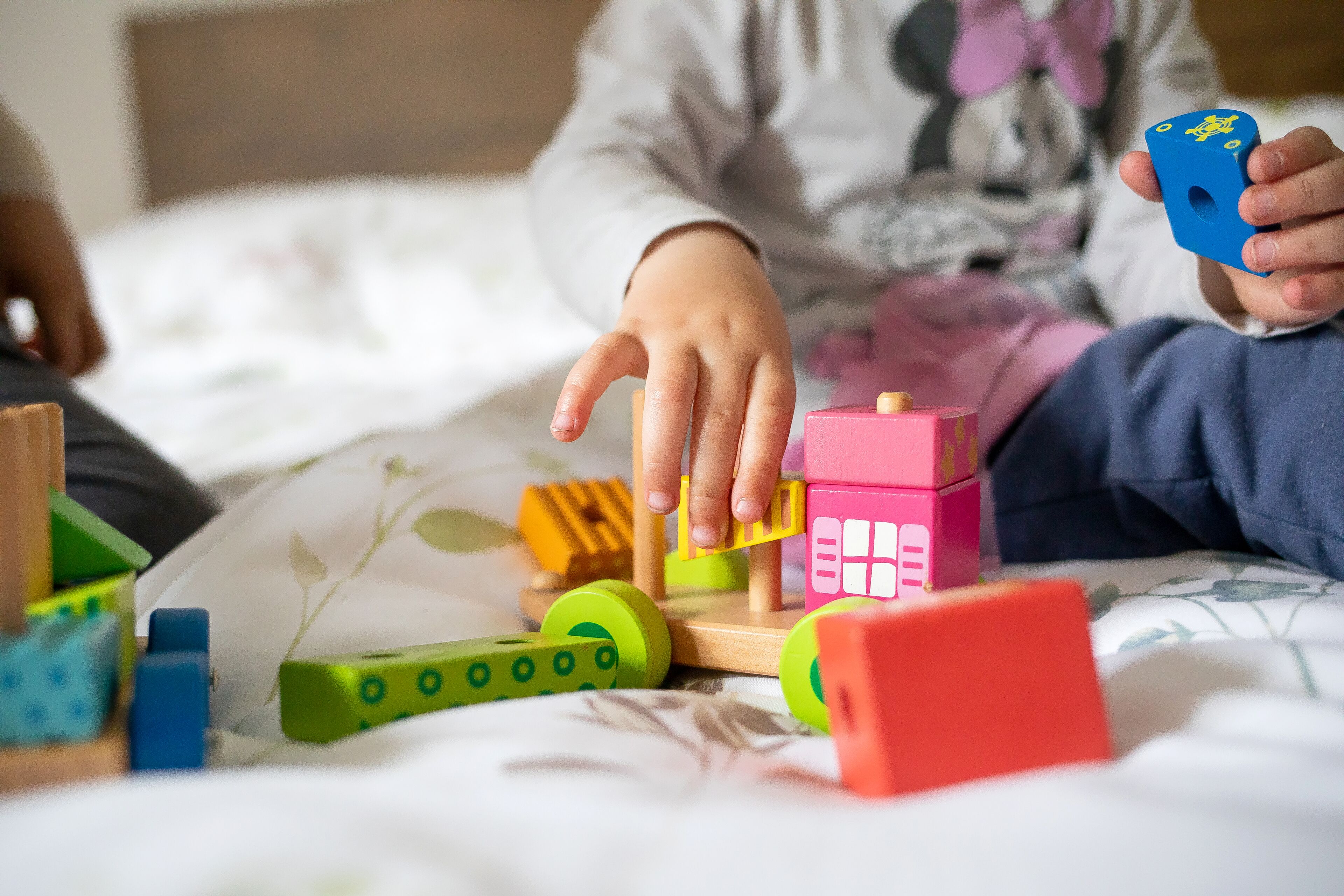 A child playing with colorful building blocks on a bed.