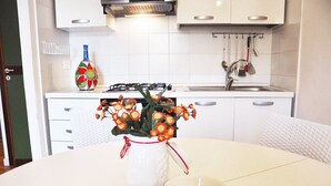 A kitchen with white cabinets, a gas stove, and a sink. There is a vase with flowers on the counter. - I tre Golfi Faro Blu (San Vito Lo Capo)