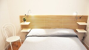 A bedroom with a wooden slat headboard, a single bed with a grey bedspread, a white chair, and bedside tables with lamps and a small plant. - I tre Golfi Faro Blu (San Vito Lo Capo)