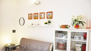 A living room with a sofa, a small table with a lamp, a cabinet with dishes, and wall-mounted artwork. - I tre Golfi Faro Blu (San Vito Lo Capo)