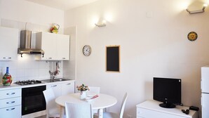 A compact kitchen with white cabinets, a gas stove, a sink, and a dining area with a white table and chairs. - I tre Golfi Faro Blu (San Vito Lo Capo)