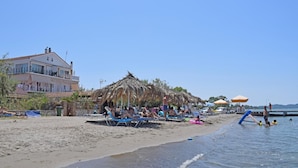 A beach with sun loungers, umbrellas, and a thatched structure. - Petrakis Beach (Corfu)